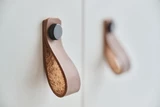 Détail de poignée en cuir avec boucle et bouton, fixée sur une porte de meuble moderne.