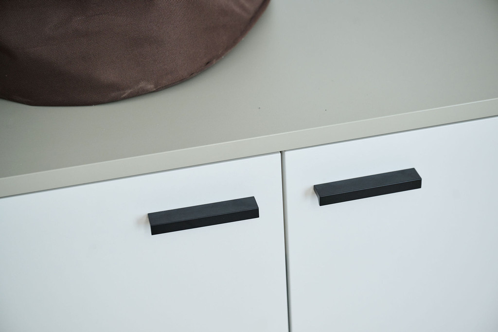Détail de portes d’armoire blanches avec poignées noires et plan de travail gris dans une buanderie moderne