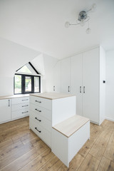 Witte dressing op maat onder een schuin dak, met een centraal eiland met lades en een zitbankje.