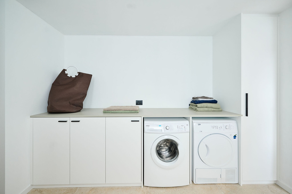 Volledig witte wasruimte met ingewerkte kasten wasmachine droogkast en werkblad in een hedendaags interieur