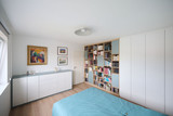 Slaapkamer met wandvullende boekenkast op maat, witte kledingkast en lage opbergkast met lades langs de tegenoverliggende wand