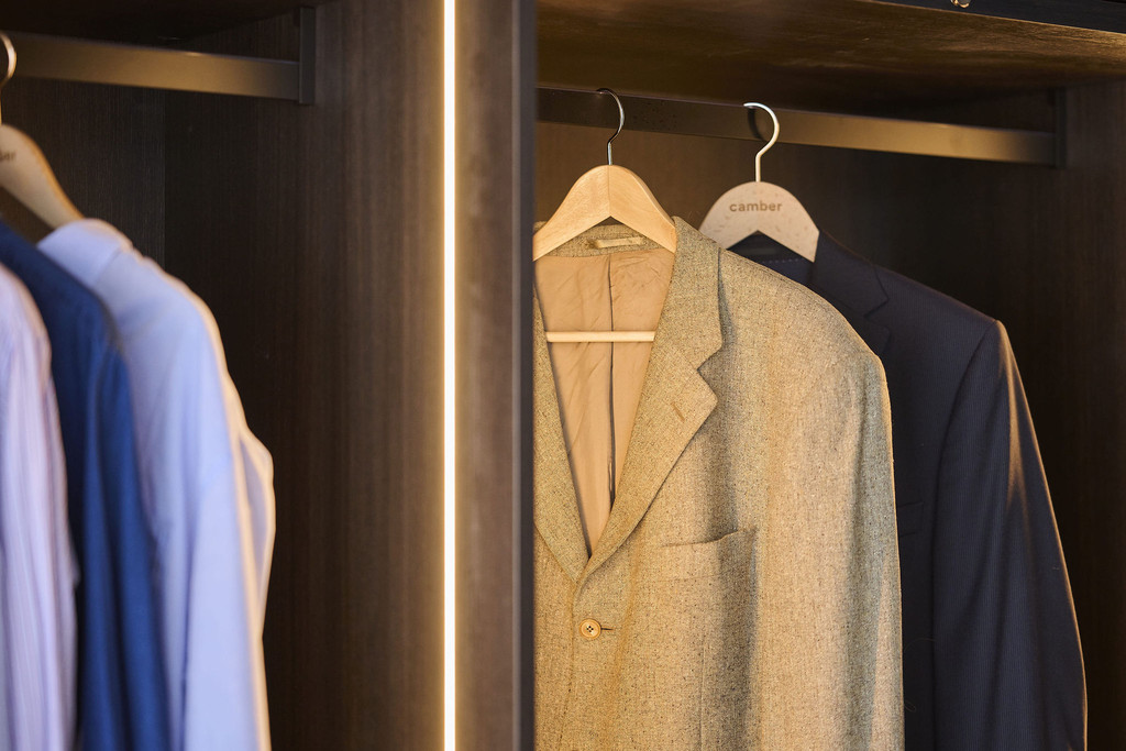 Penderie dans un dressing sur mesure avec vêtements et éclairage LED vertical en bois foncé en showroom