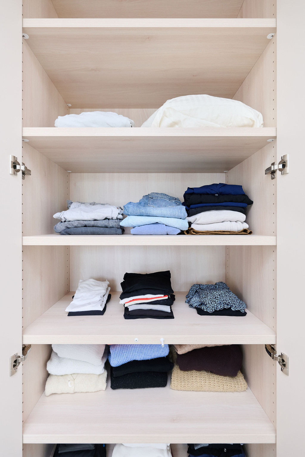 Armoire ouverte avec vêtements pliés sur trois étagères en bois dans une chambre lumineuse