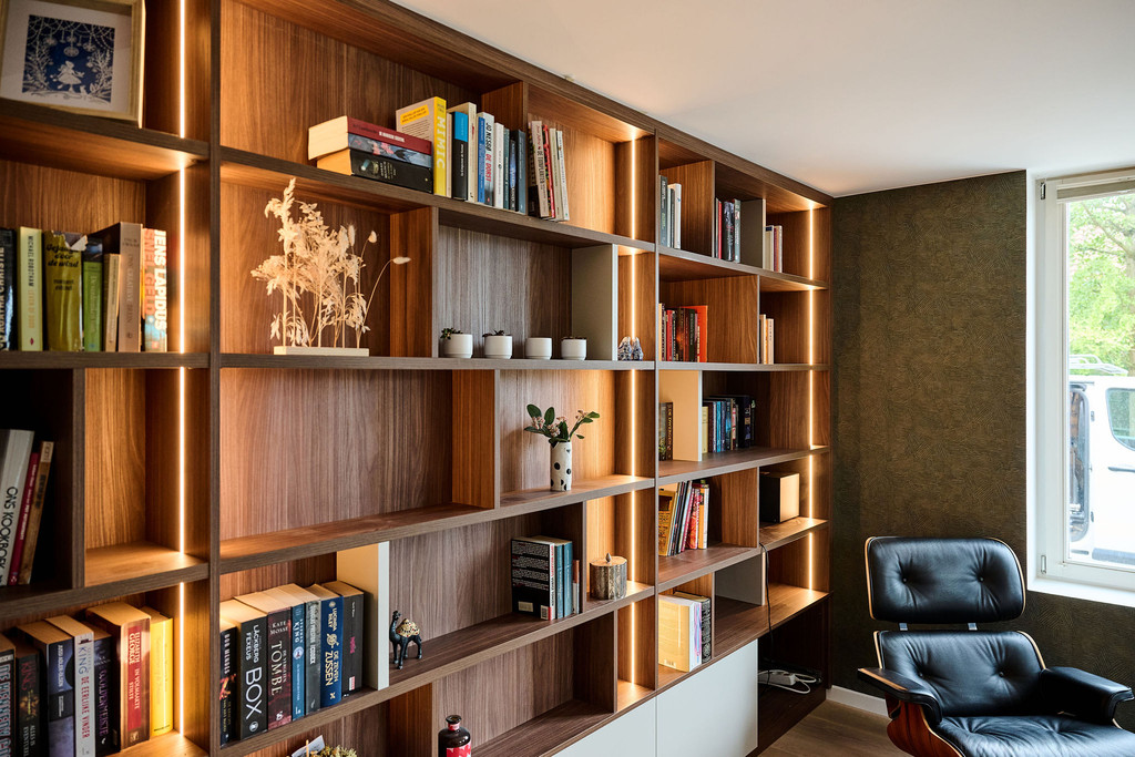 Houten boekenkast op maat met ingebouwde verlichting en open vakken gevuld met boeken en decoratie