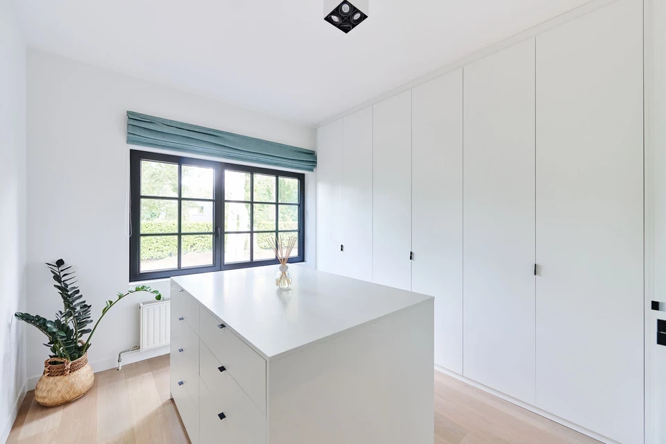 Armoire dressing blanche sur mesure avec îlot central et poignées noires fines dans une pièce lumineuse