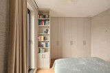 Dressing sur mesure avec portes en tons clairs et bibliothèque ouverte intégrée près de la fenêtre, combinant rangement et espace pour livres dans une chambre lumineuse, réalisé par Camber