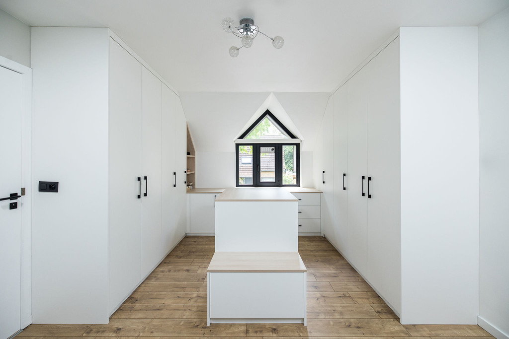 Dressing encastrée blanche avec îlot central et banc intégré sous une fenêtre en pente, sol en bois