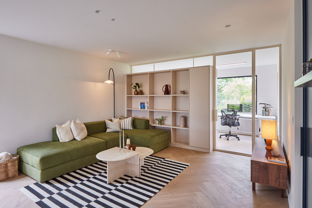 Ingerichte woonkamer met maatwerkboekenkast, groene sofa en veel daglicht