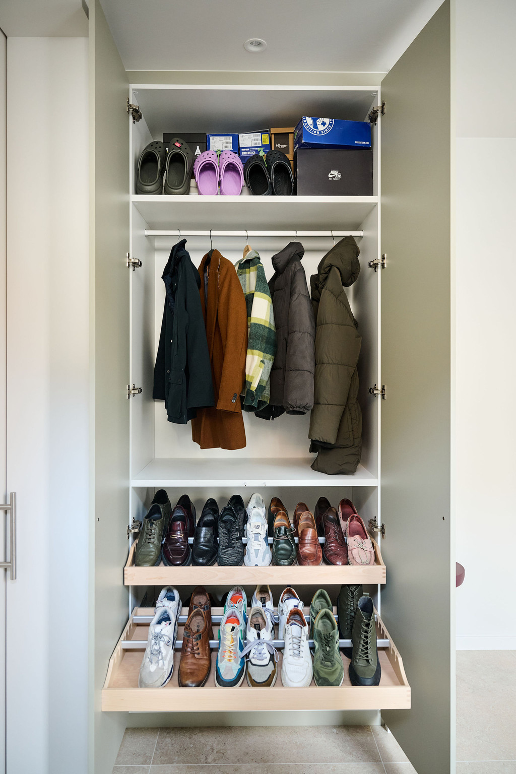 Armoire d’entrée blanche ouverte avec manteaux suspendus et plusieurs paires de chaussures sur étagères