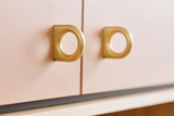 poignées dorées arrondies fixées sur des portes de placard rose pâle avec un socle en bois clair.
