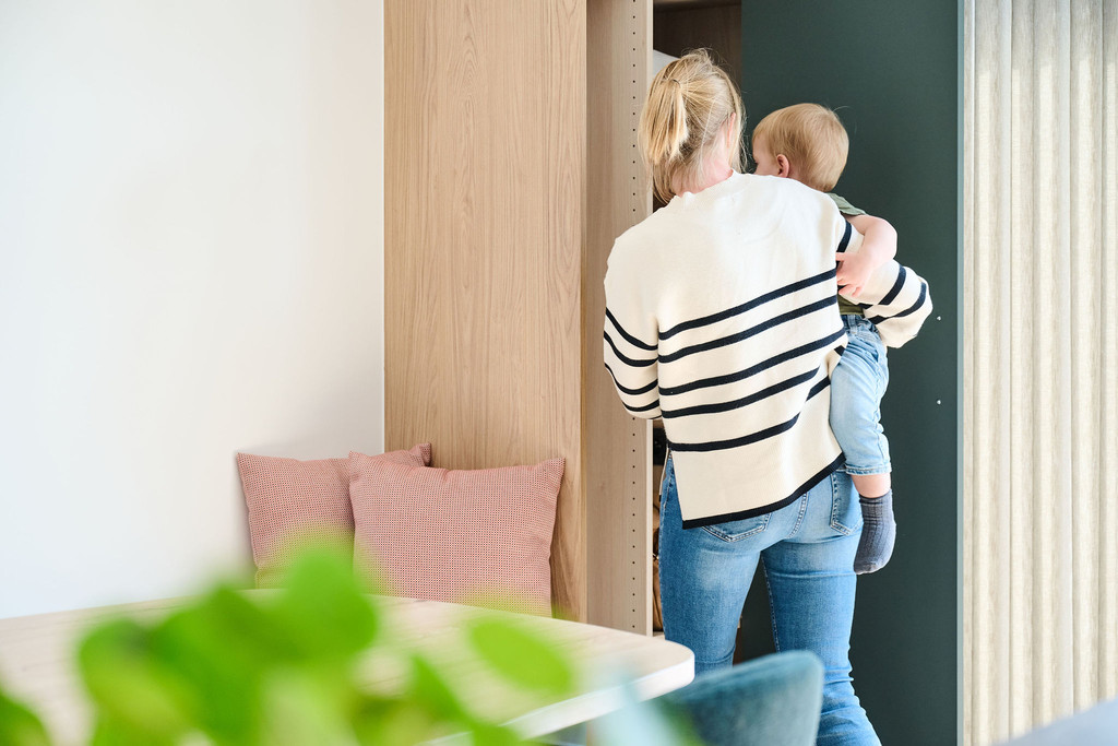 Femme portant un enfant dans un salon avec coussins roses et meuble vert