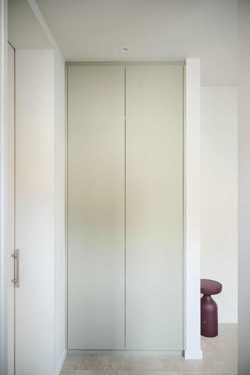 Armoire blanche sur mesure fermée et encastrée dans une niche entre deux murs dans un hall d’entrée moderne