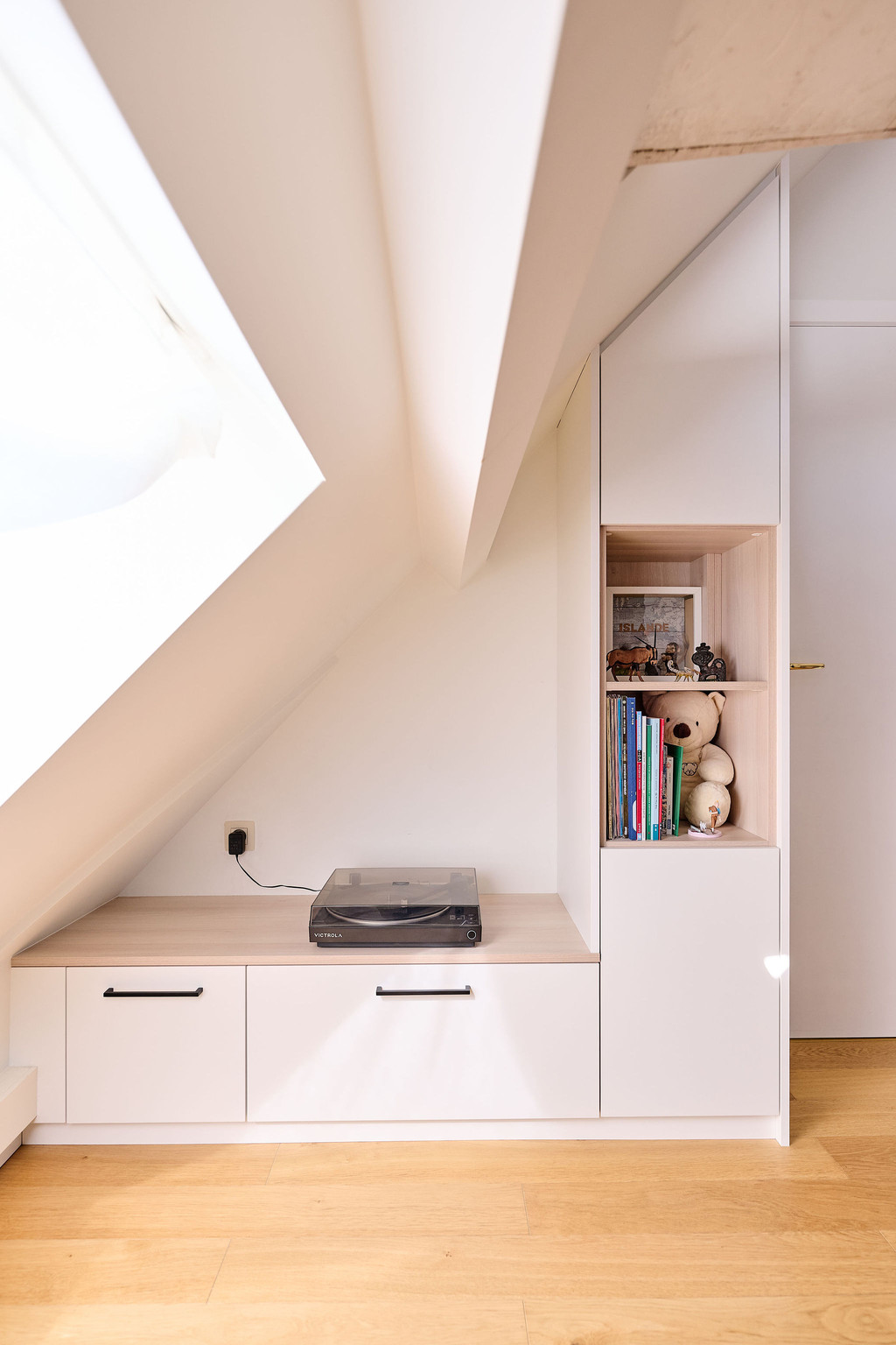 Meuble bas sur mesure sous pente avec tiroirs, niche ouverte et plateau en bois dans une chambre d’enfant