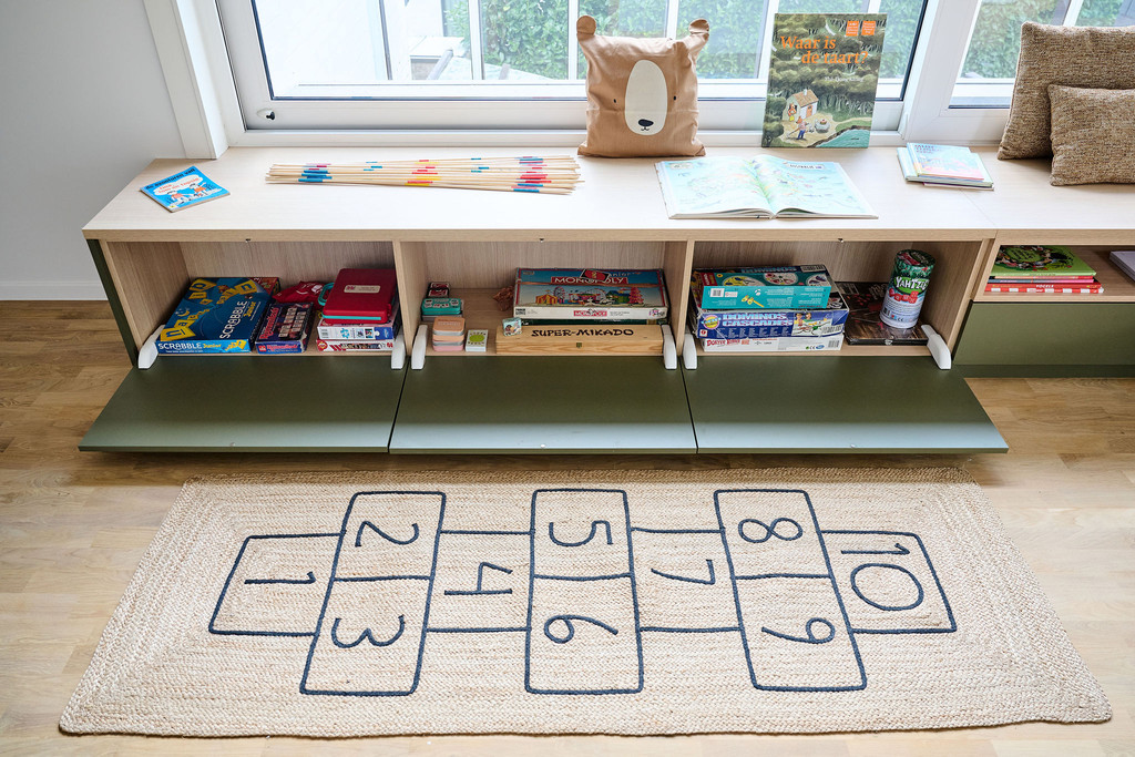 Open zitbank op maat onder raam met kinderboeken en spelletjes boven een hinkelspelmat