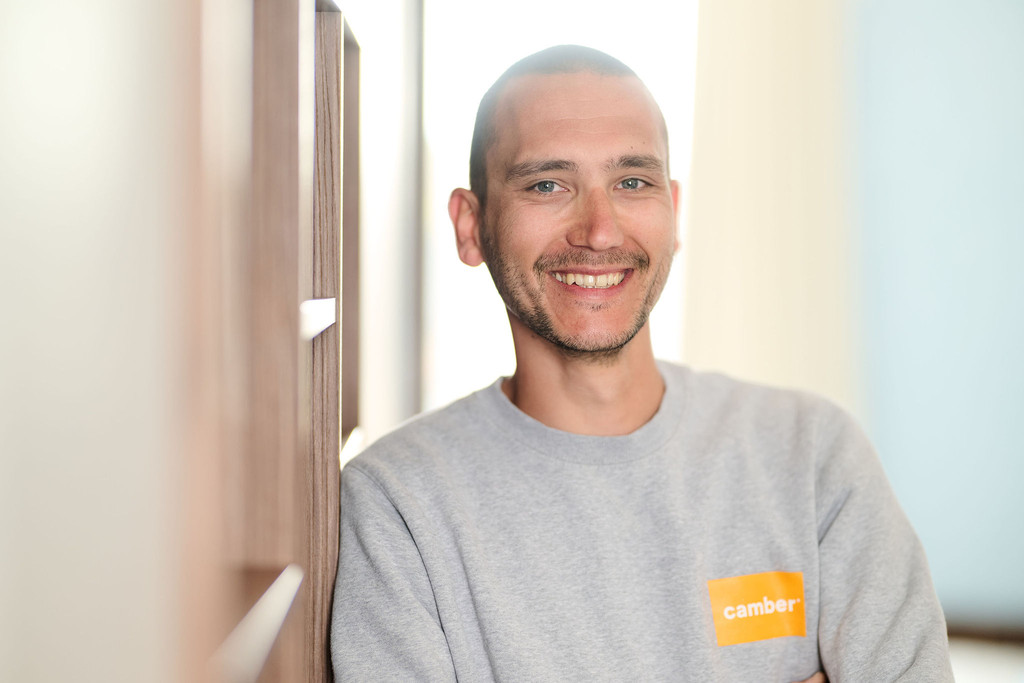 Menuisier Camber souriant appuyé contre un meuble sur mesure, illustrant le savoir-faire et la qualité de réalisation des projets personnalisés