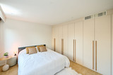 Chambre avec placards blancs sur mesure couvrant tout un mur, longues poignées en bois et lit double avec coussins beiges