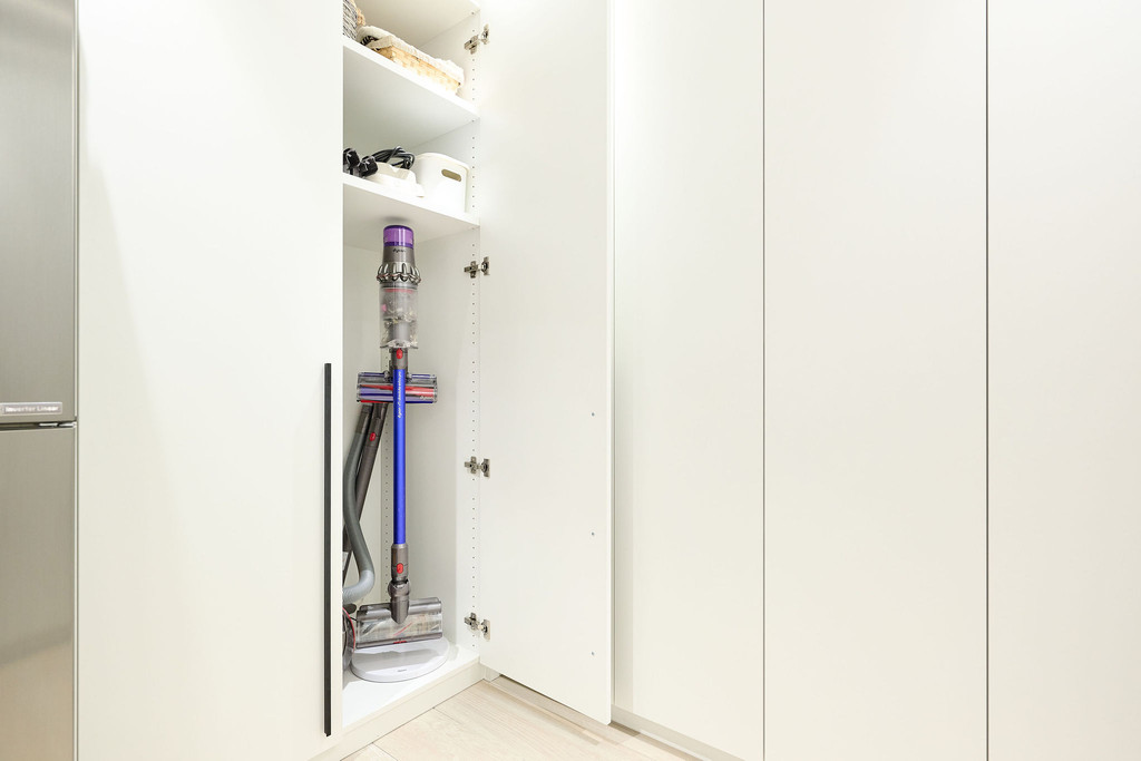 Rangement dans une armoire blanche sur mesure avec un aspirateur sans fil et étagères pour produits de nettoyage.