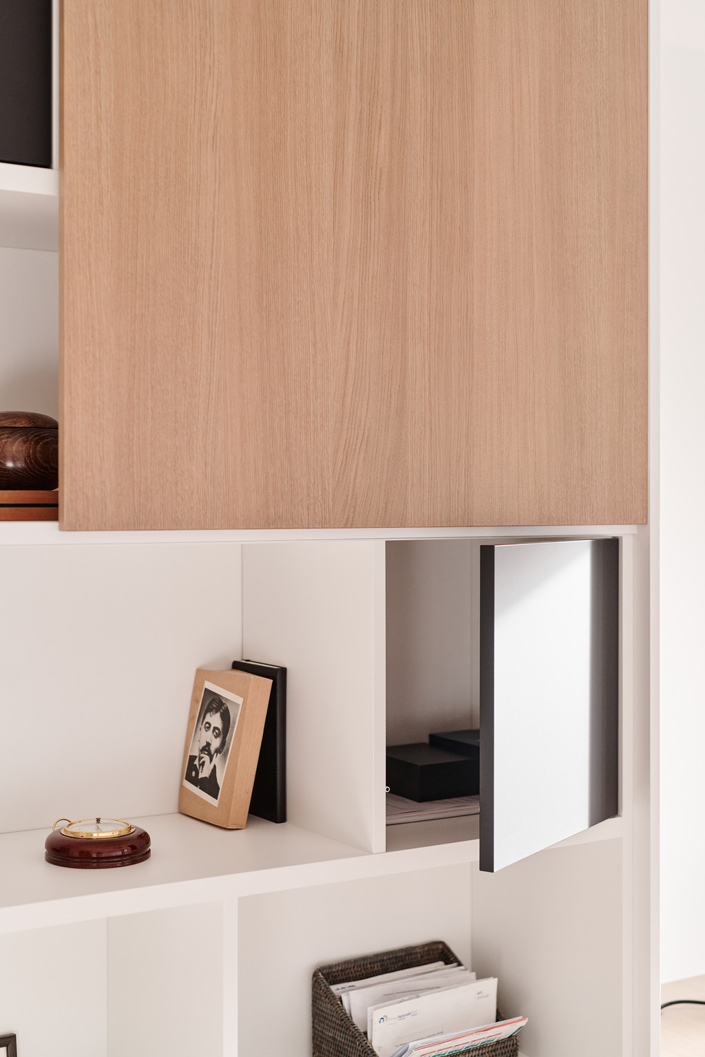 Bibliothèque sur mesure avec niches blanches et bois, porte coulissante en métal ouverte dévoilant un espace de rangement discret.