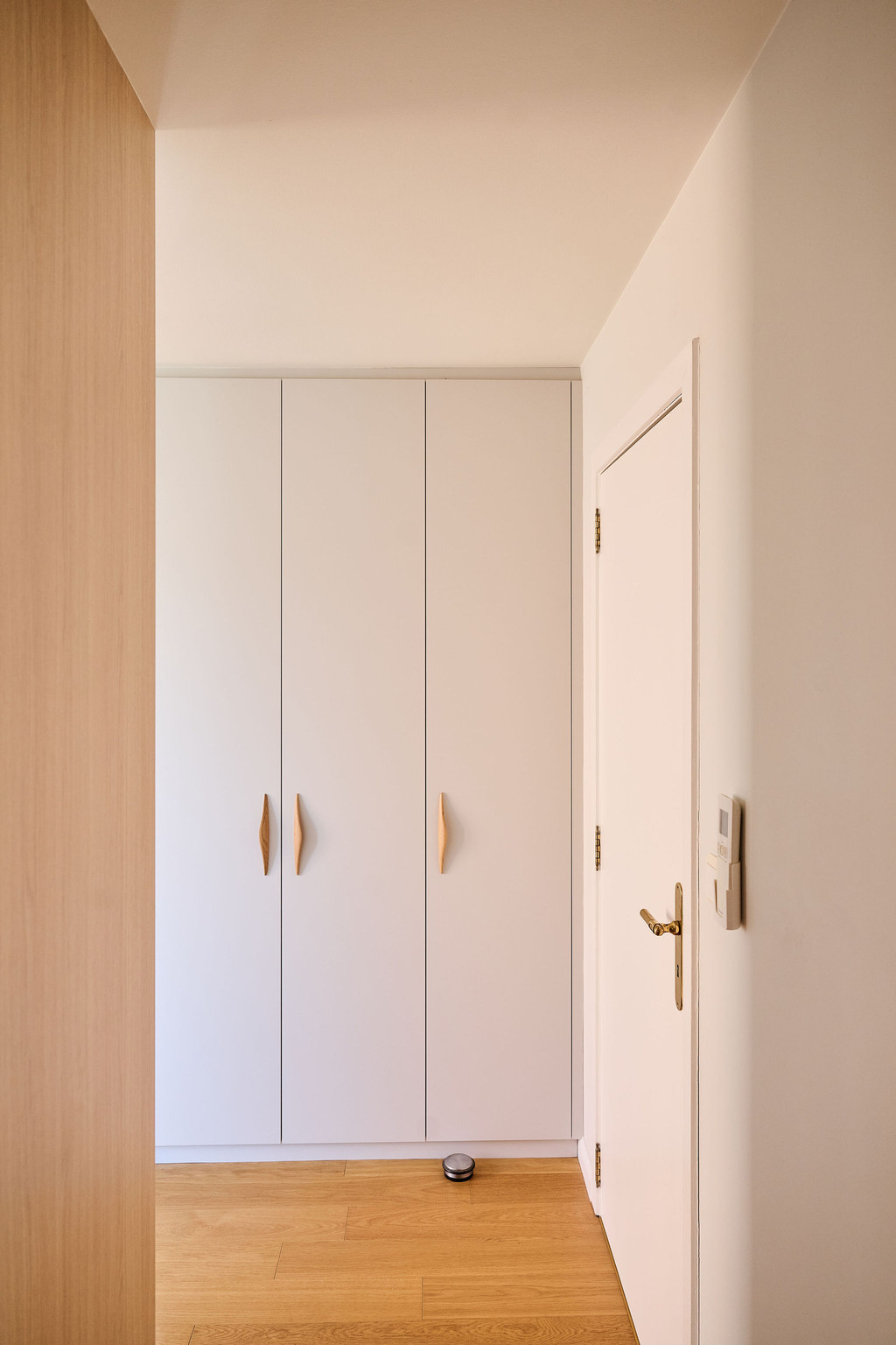 Placard sur mesure intégré avec portes blanches et poignées en bois dans une chambre lumineuse