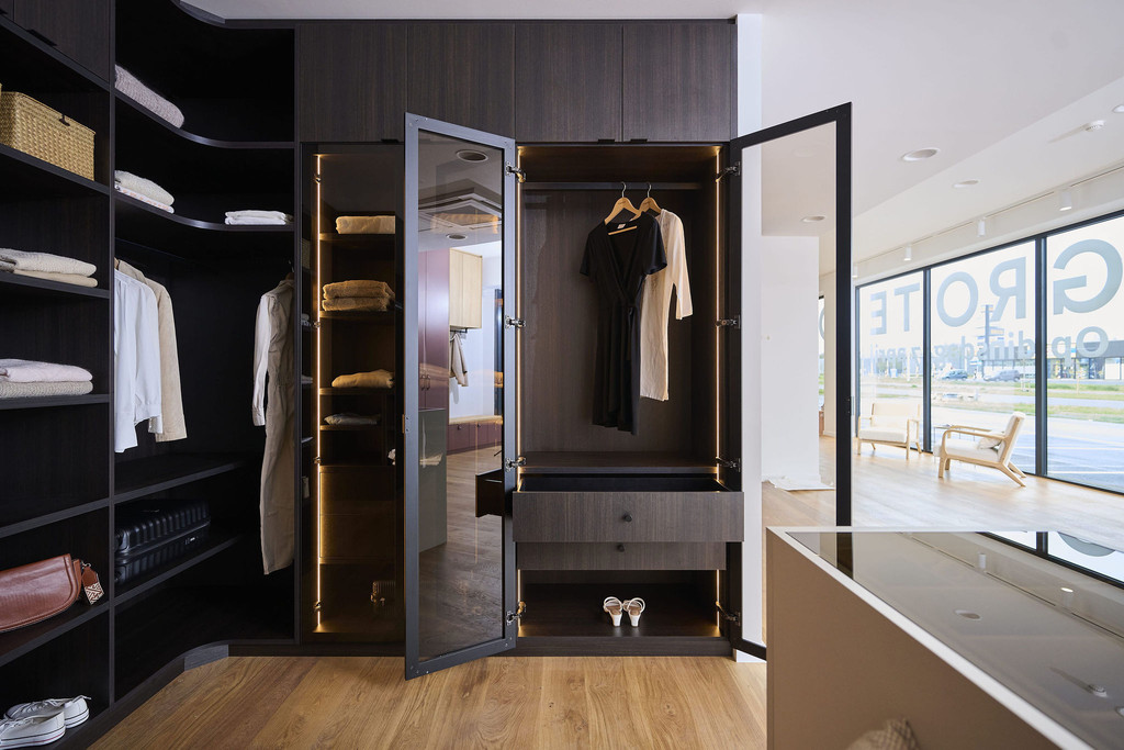 Dressing sur mesure avec portes miroir, penderie et tiroirs en bois foncé dans un showroom