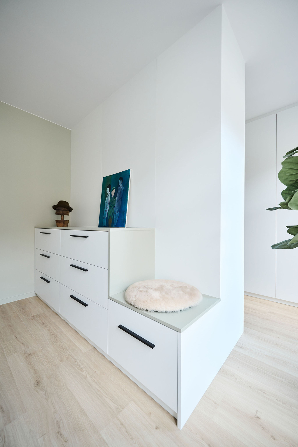Witte maatkast met lades en geïntegreerd zitbankje in een lichte kamer met houten vloer en decoratieve accenten