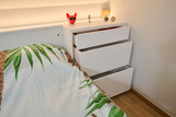 Détail d'une commode moderne avec trois tiroirs, à côté d'un lit d'enfant avec une couverture aux motifs de feuilles.