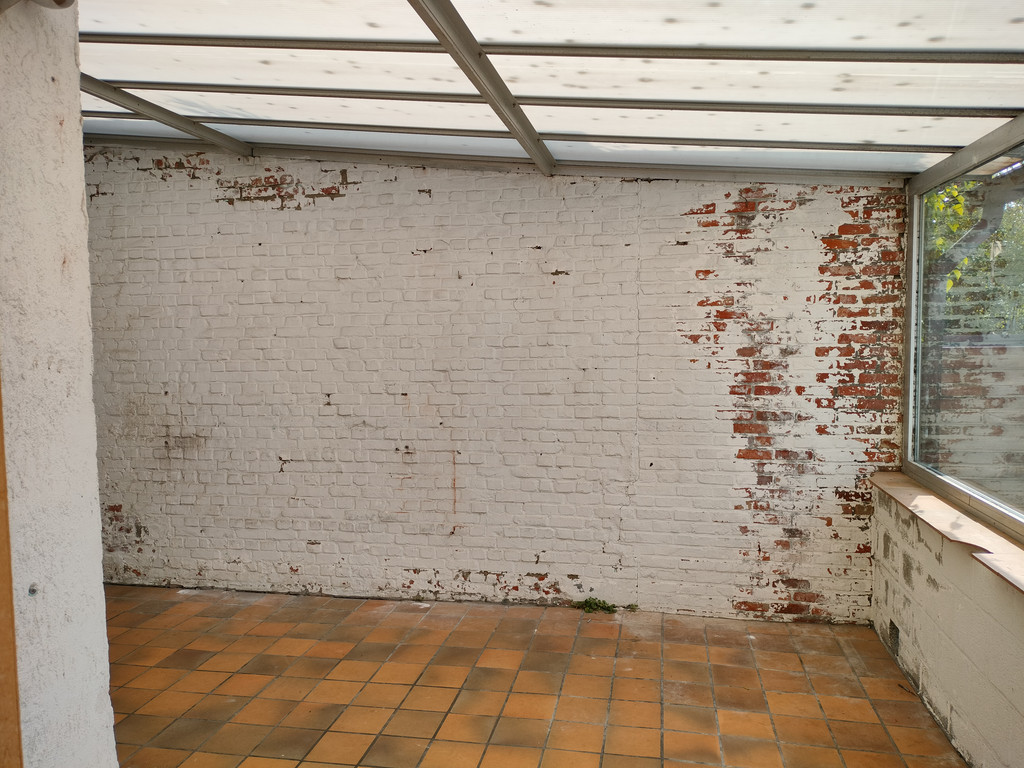 Mur en briques partiellement peintes avec carrelage orange dans un espace avant rénovation