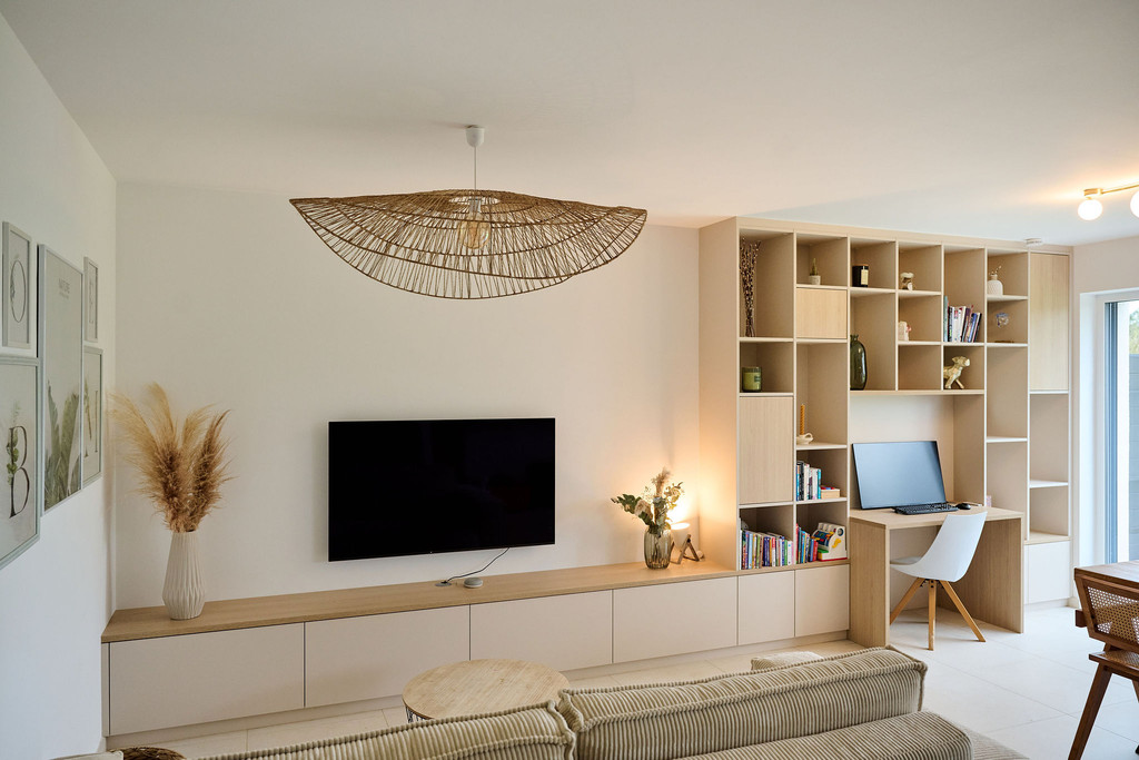 Meuble TV sur mesure avec un coin bureau, étagères ouvertes et placards, fauteuil et décoration moderne dans un salon lumineux.