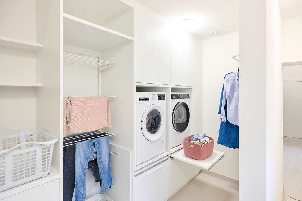 Buanderie sur mesure avec machine à laver, sèche-linge, étagères de rangement et espace pour suspendre les vêtements.