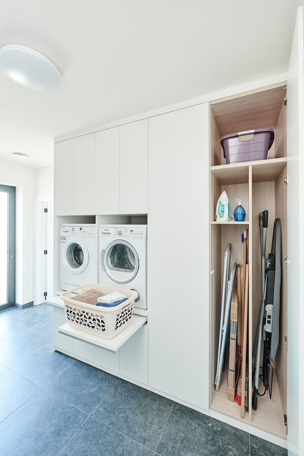 Wasruimte op maat met wasmachine en ruimte voor schoonmaakmaterialen zoals bezems en emmers.
