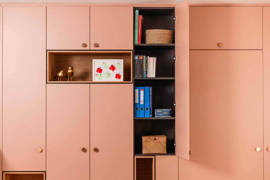 Een roze maatkast met open nissen, boeken, manden en een kindertekening als decoratie. De opstelling straalt warmte en orde uit dankzij de combinatie van hout en roze tinten.