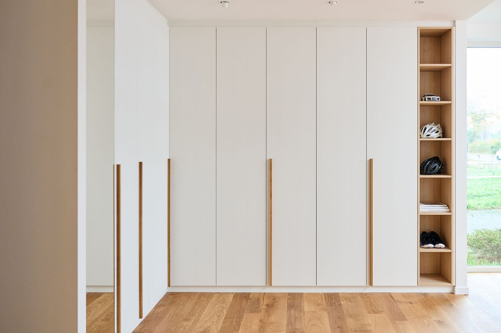 Dressing sur mesure avec portes blanches et poignées verticales en bois clair, design minimaliste et élégant.