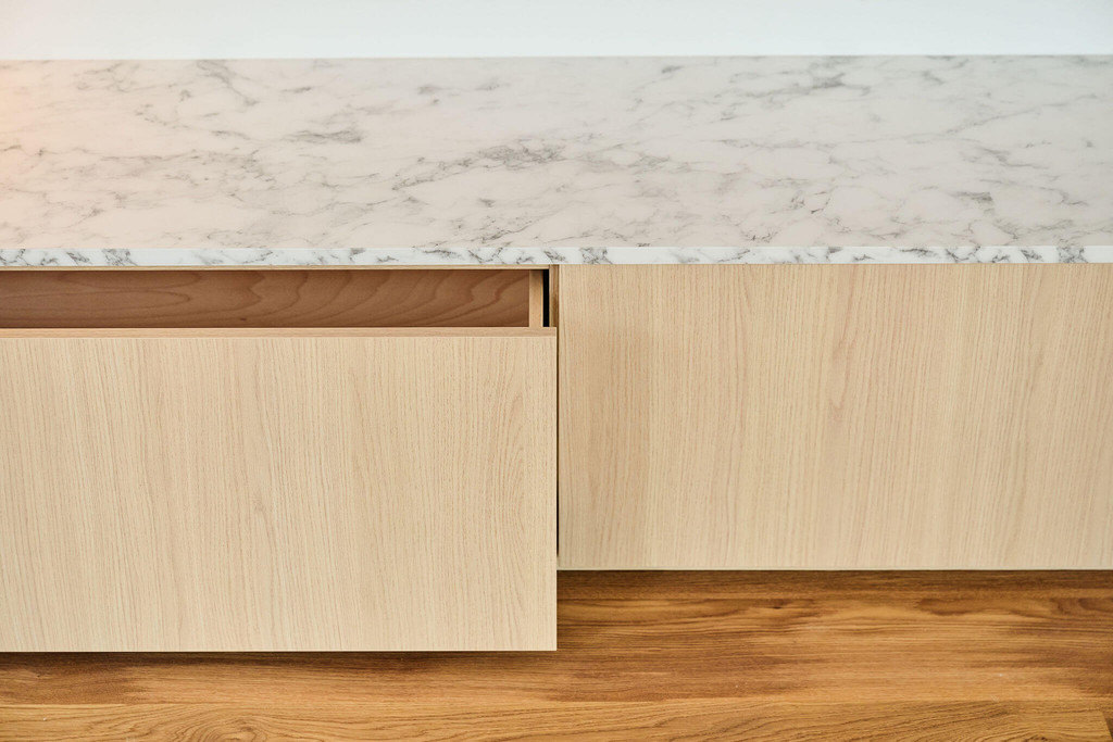 Rangement sur mesure dans le salon avec des tiroirs en teinte de bois clair et tablette aspect marbre