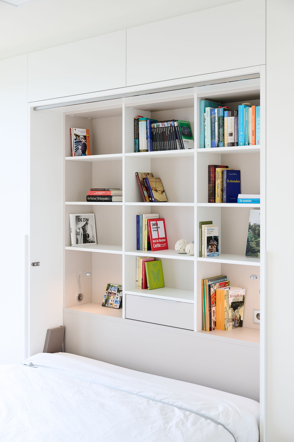 Opklapbed met ingebouwde boekenkast, boeken netjes opgevouwen in de planken, met een opbergvak onderaan.