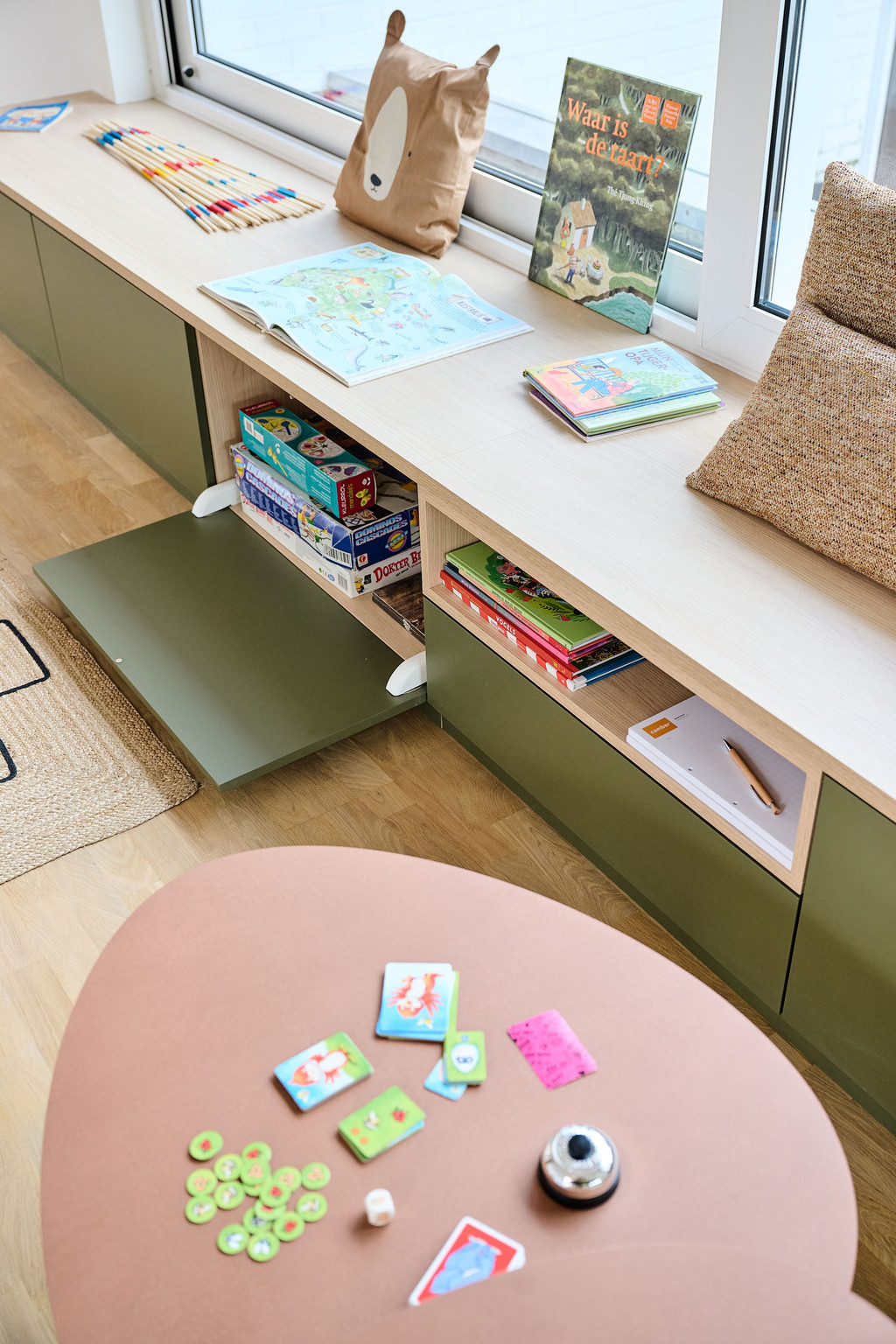 Laag zitmeubel op maat met open vakken gevuld met kinderboeken en spelletjes