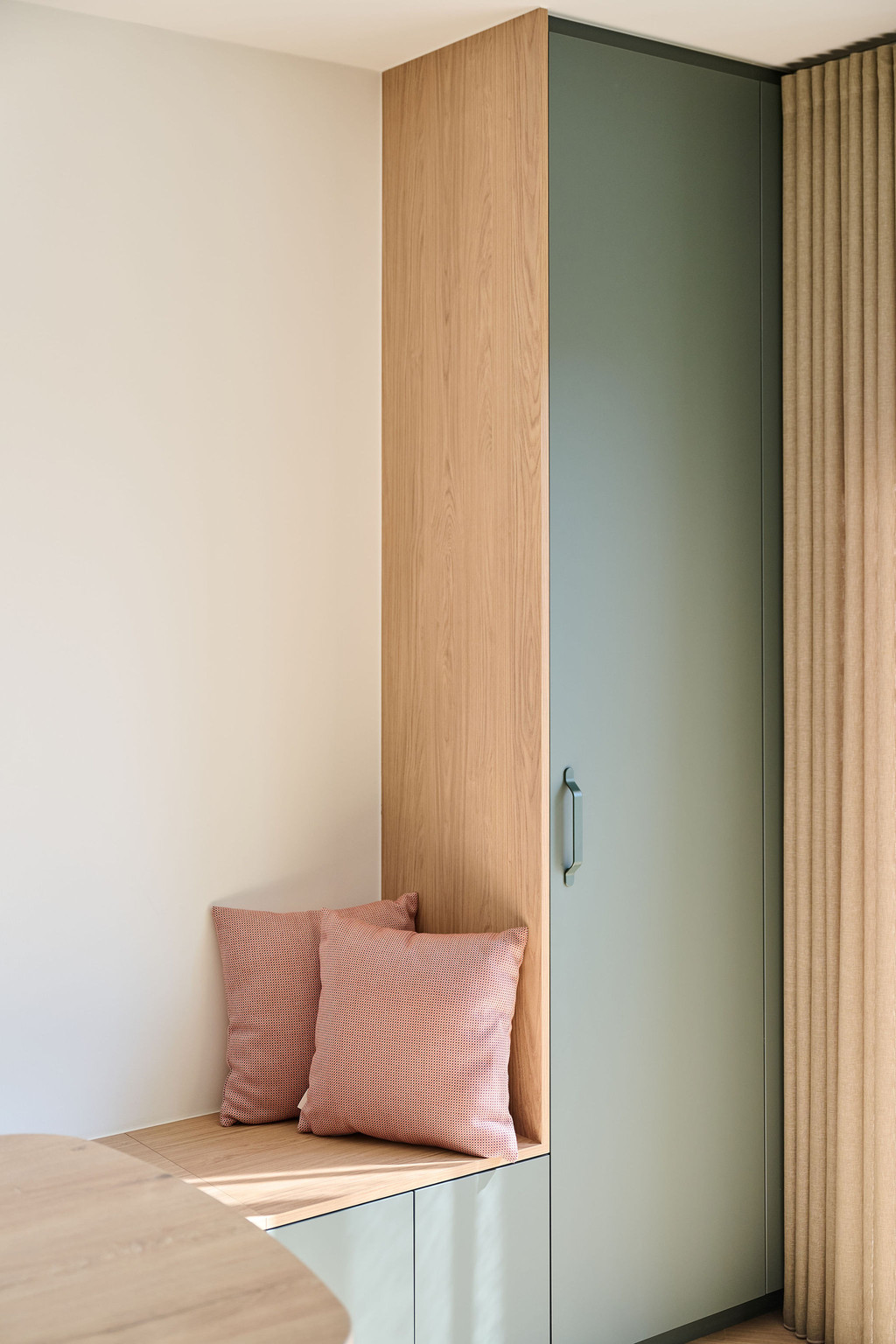 Placard vert mat avec poignée verticale et coussins roses sur banc en bois clair
