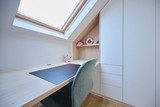 Détail d'un bureau dans une chambre d'enfant sous pente avec étagères et fauteuil confortable.