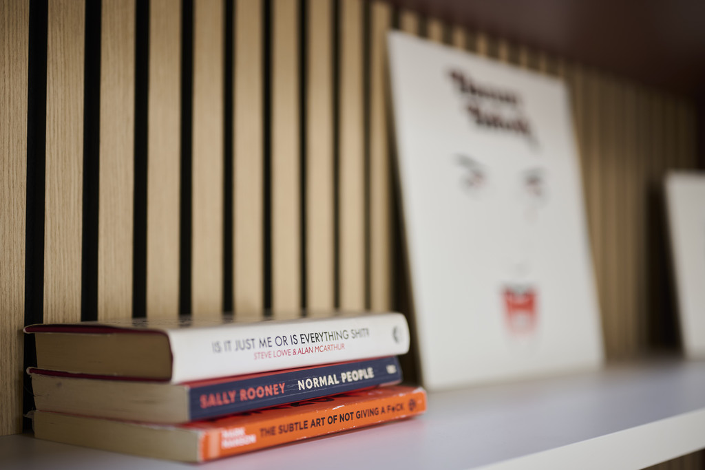 Détail d’un panneau à lattes en bois avec étagère blanche contenant des livres et objets décoratifs