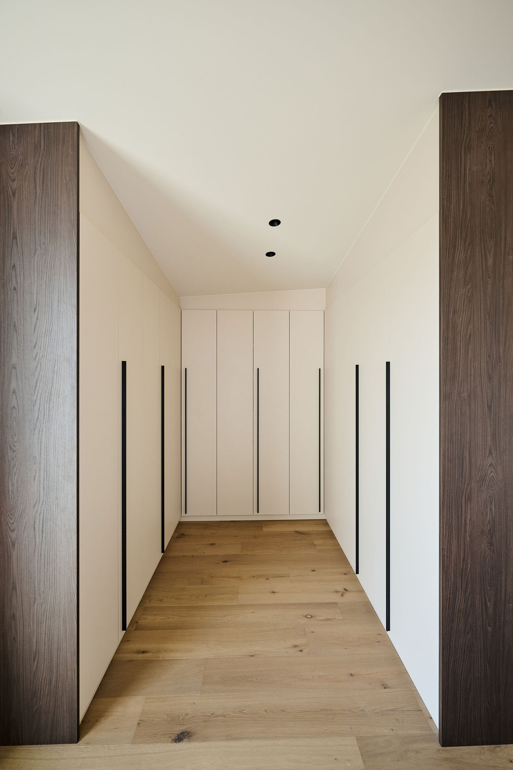 Dressing sur mesure en U avec portes en tons clairs et longues poignées, offrant un espace de rangement structuré et élégant, réalisé par Camber