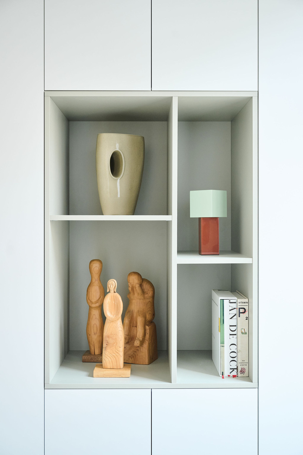 Gros plan sur niches ouvertes d’une armoire blanche avec sculptures en bois vase lampe et livres