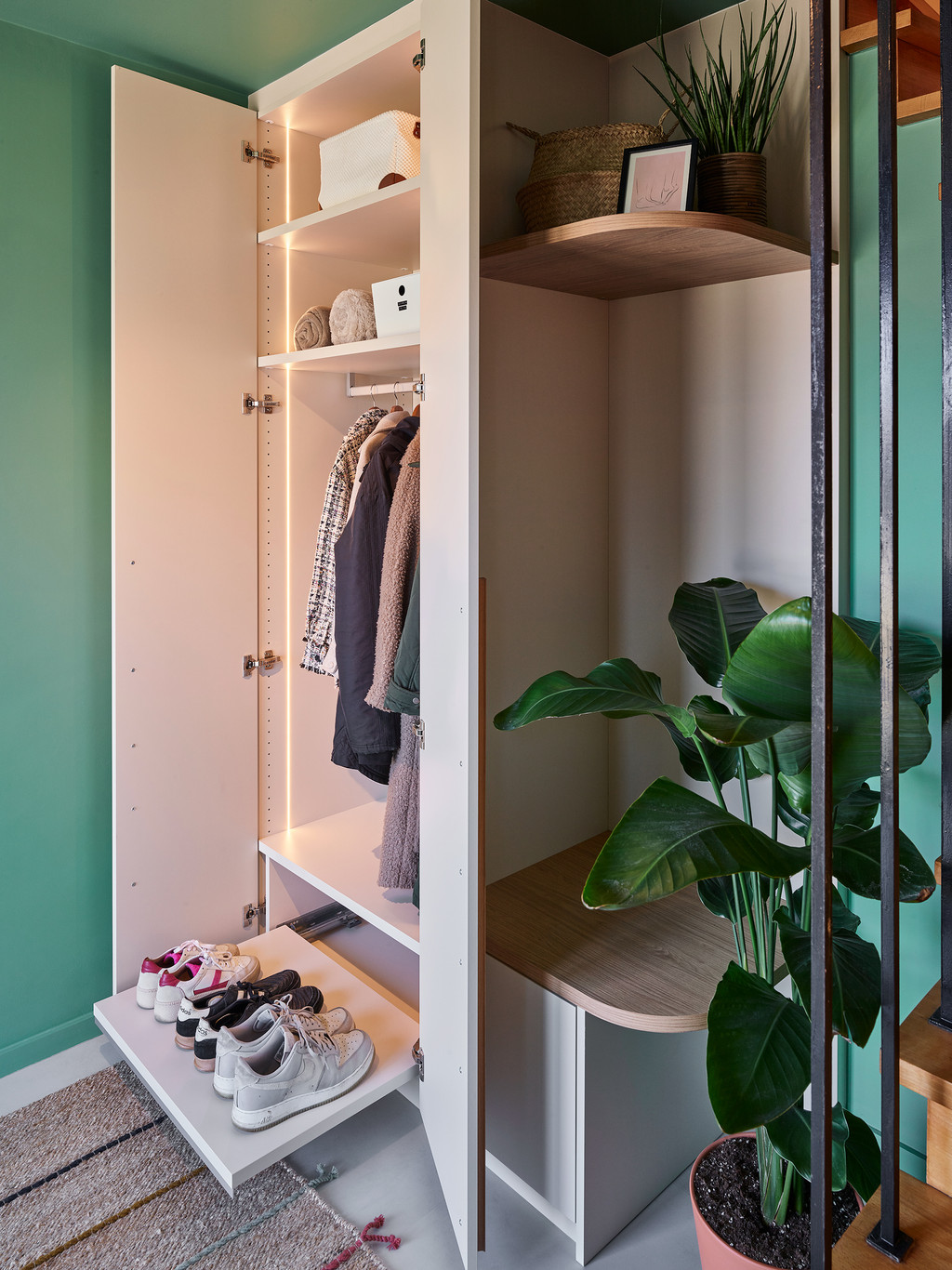 Open inkomkast op maat met verlichting, kleding en schoenen naast grote groene plant