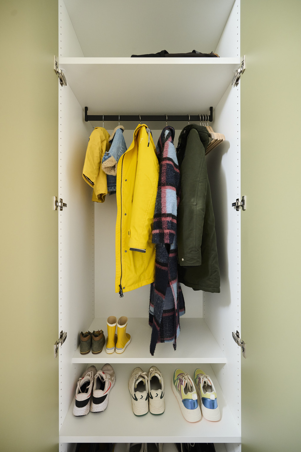 Open maatkast in groene inkomhal met jassen, schoenen en wandkapstok