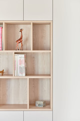 Bibliothèque sur mesure en bois clair avec niches ouvertes décorées de livres, objets de décoration et une figurine de girafe.