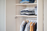 Armoire ouverte sur mesure avec étagères et tringle remplie de vêtements pliés et suspendus