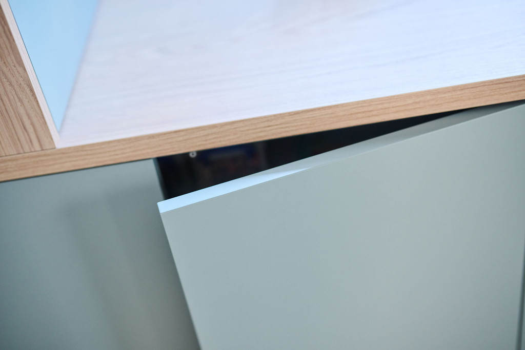 Detail van greeploos kastdeurtje onder licht houten bureaublad in blauw maatmeubel
