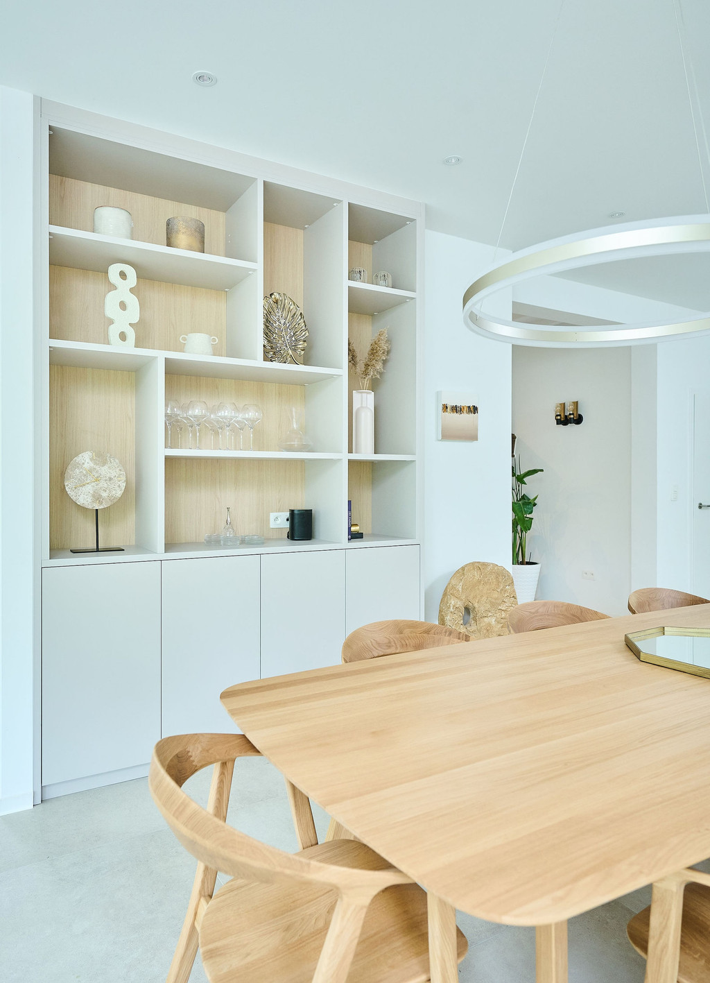 Meuble sur mesure avec étagères ouvertes en bois clair et compartiments fermés, décoré avec des objets modernes et un espace repas avec table en bois.