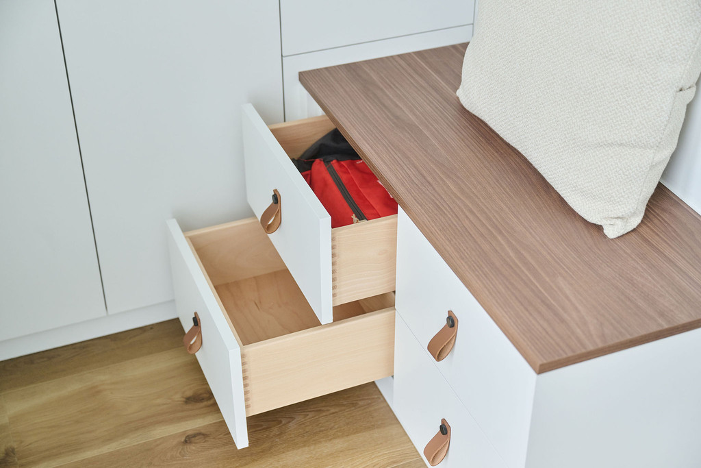 Détail d'un meuble de vestiaire sur mesure avec tiroirs ouverts, rangement de chaussures et poignées en cuir.