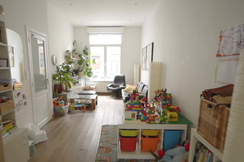 Salon familial avant transformation, avec jouets pour enfants, plantes et coin bureau
