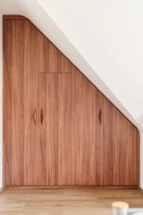 Dressingkast op maat onder schuin dak met houten afwerking en geïntegreerde deuren voor een naadloze look.