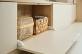 Détail d'un meuble TV sur mesure avec porte abattante, mettant en valeur des paniers en osier pour un rangement pratique et esthétique.